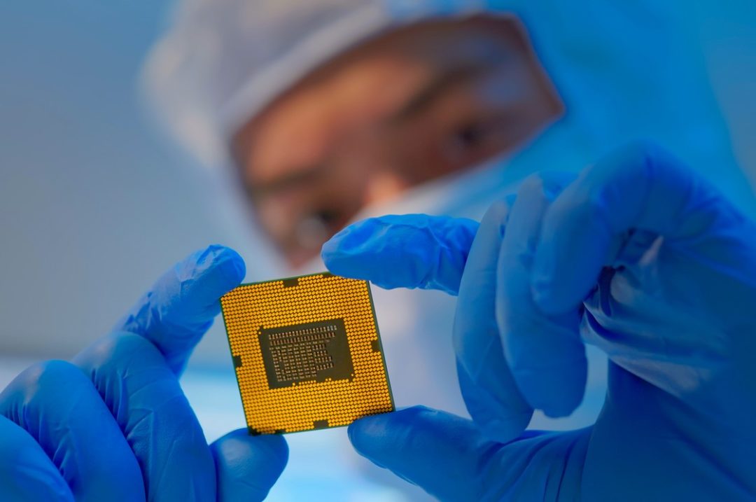 A WORKER WITH RUBBER GLOVED HANDS EXAMINES A SEMICONDUCTOR CHIP